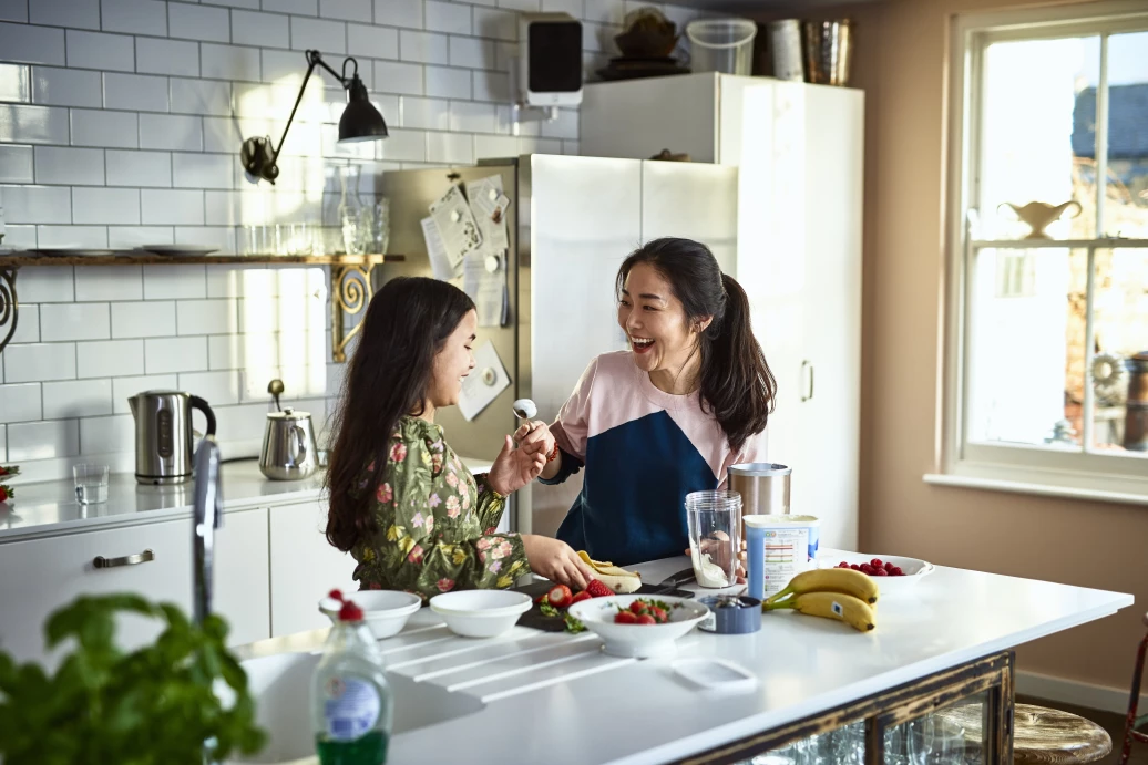 Mother teasing daughter in kitchen while making smoothies